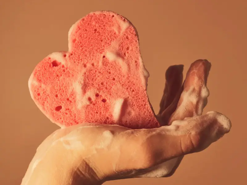 A cute sponge in the hand of a woman. Cold showers are how to holistically aid muscle recovery.